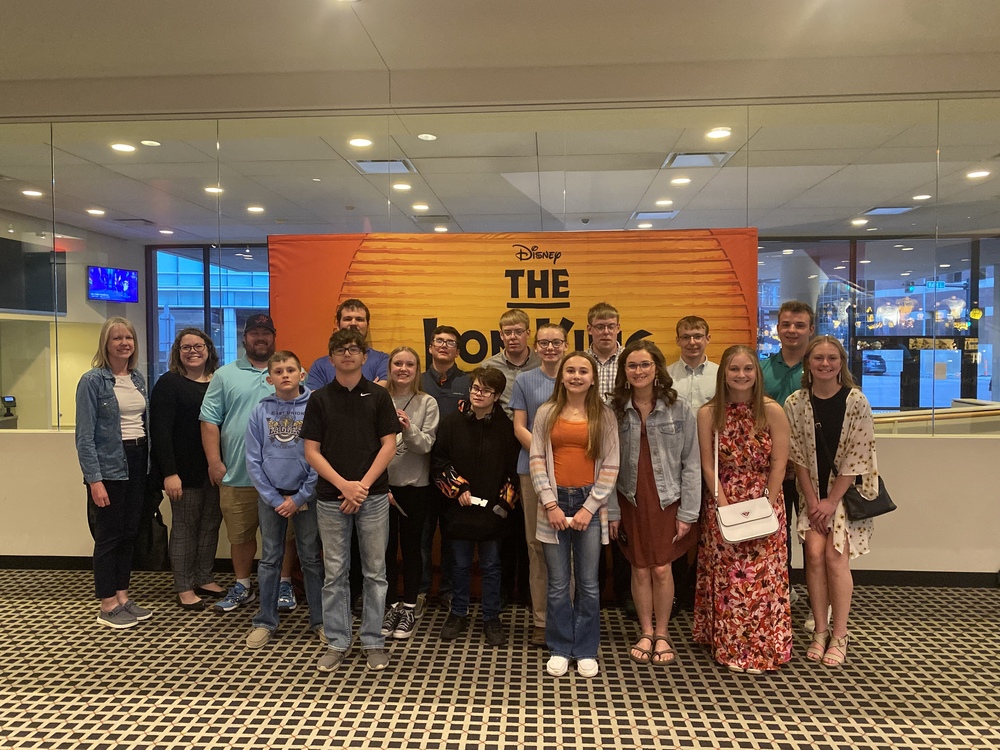 Students and sponsors in front of Lion King poster.