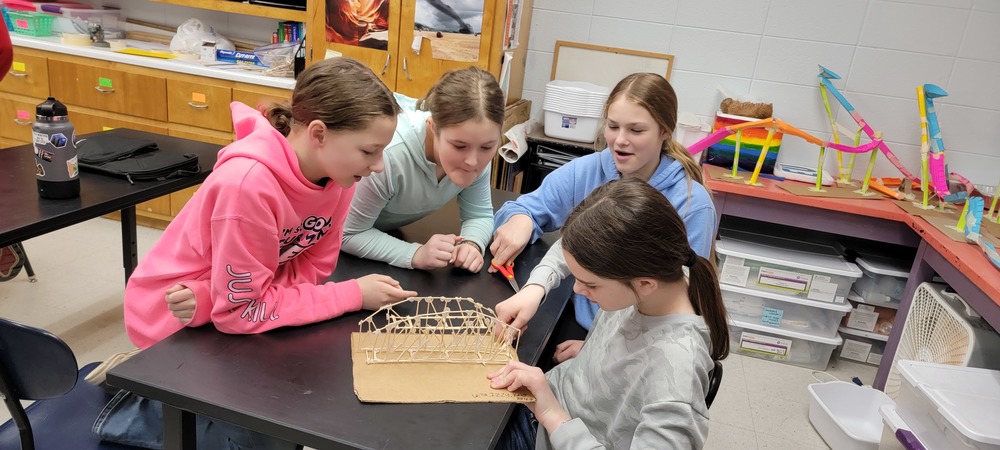 Four girls building a toothpick bridge.